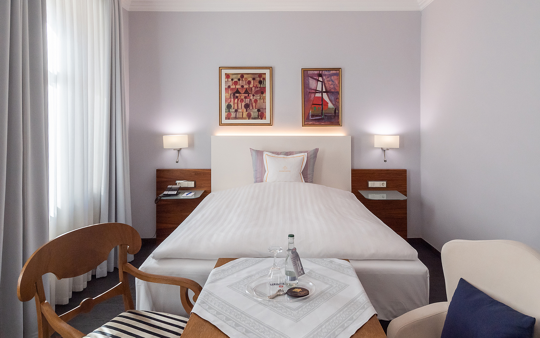 Ein ordentlich gemachtes Einzelbett in einem gemütlichen, modernen Hotelzimmer in Fulda mit minimalistischer Einrichtung, zwei gerahmten Gemälden und idealer Ausstattung für Ihre nächste Tagung.