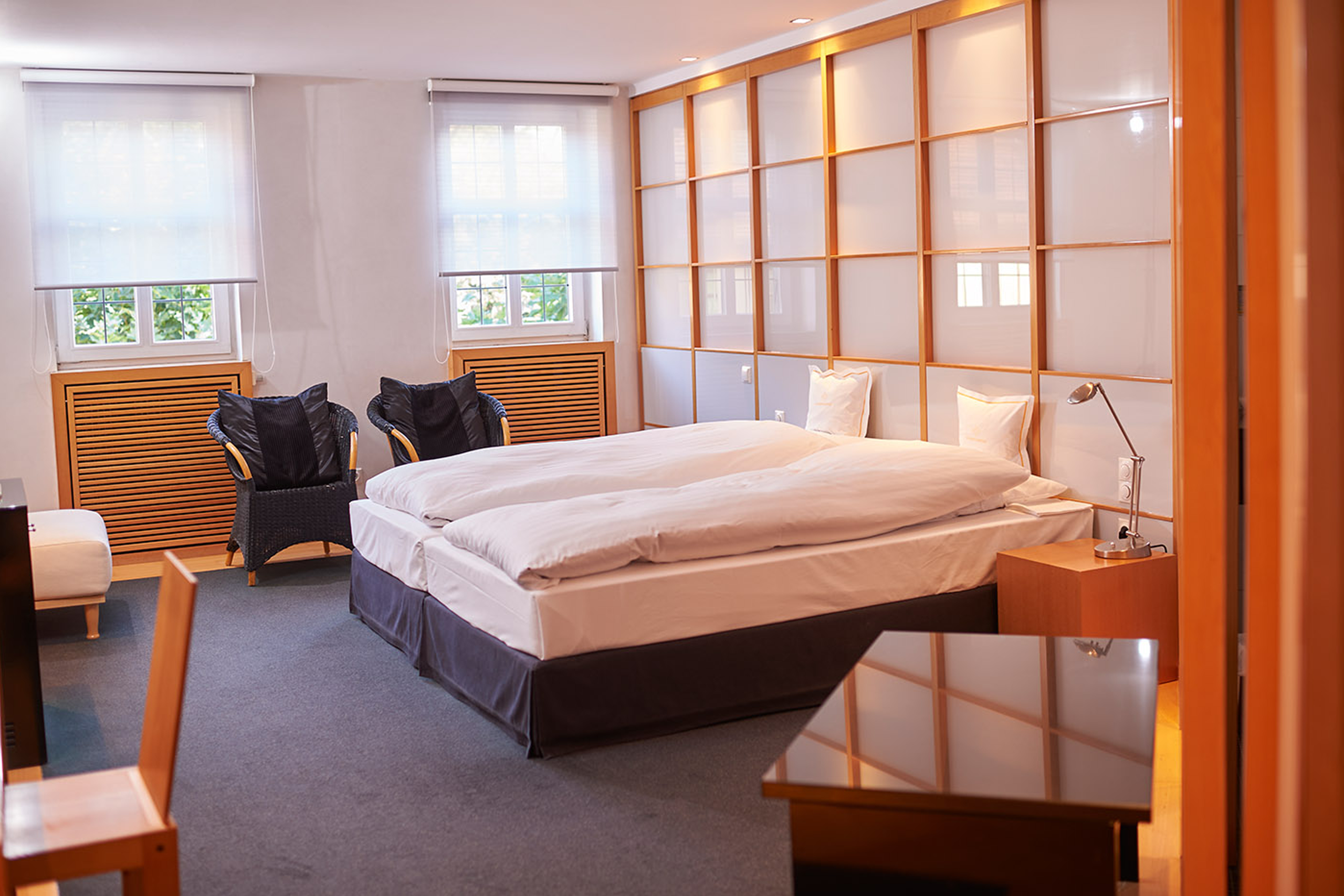 Modernes Hotelzimmer mit Doppelbett, Sesseln am Fenster und Holzakzenten.