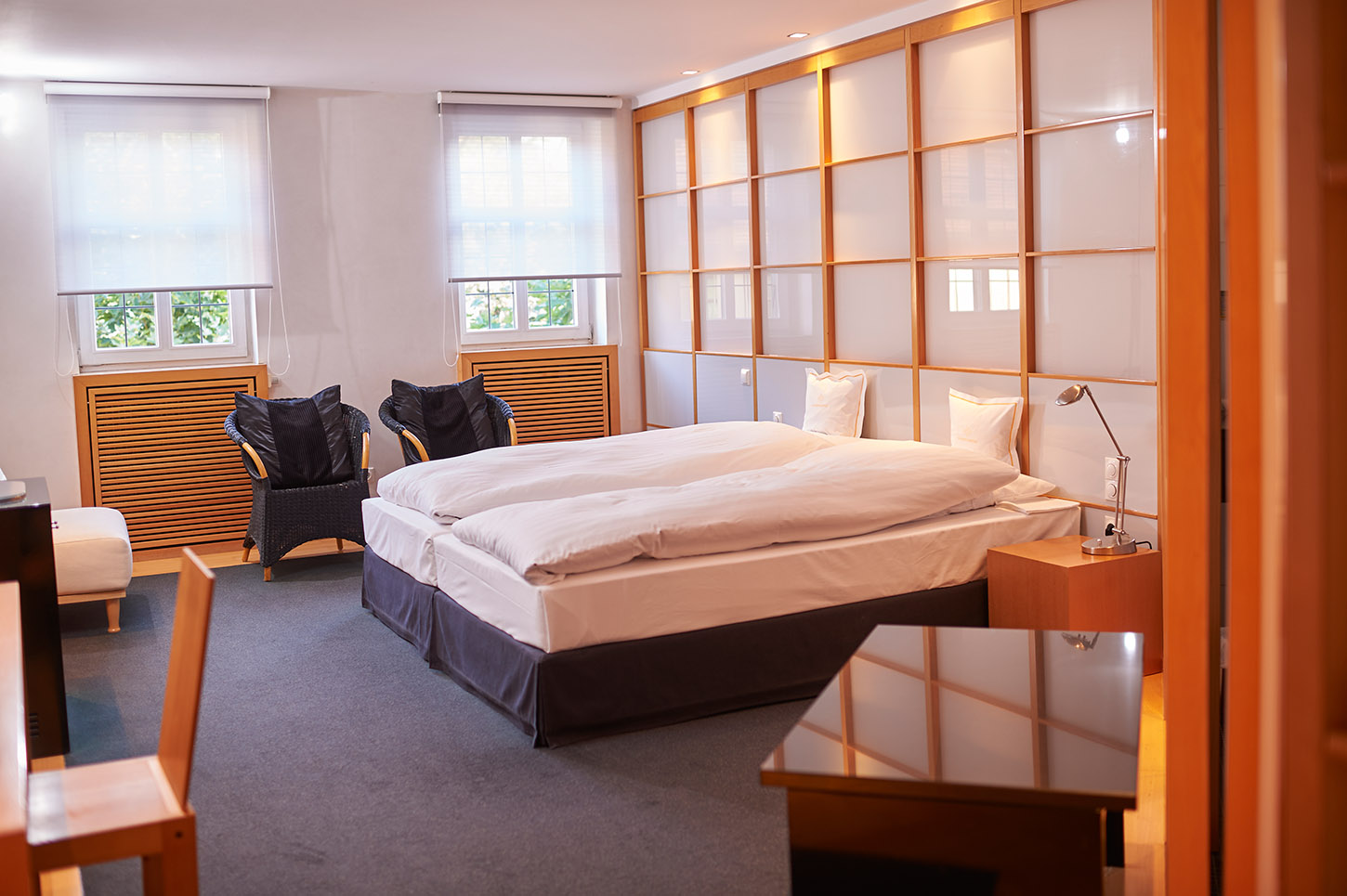 Helles Hotelzimmer im Goldenen Karpfen in Fulda mit Doppelbett, Korbstühlen, großen Fenstern und moderner Holzeinrichtung – ein idealer Rückzugsort nach einer erfolgreichen Tagung.