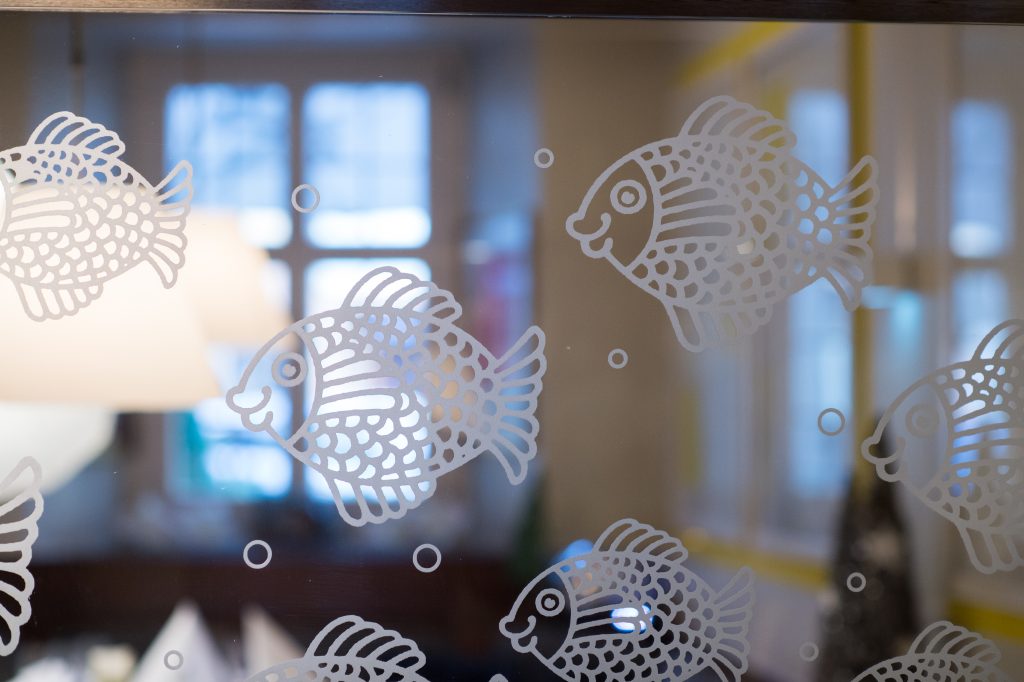 Weiße Fischaufkleber auf einem Glasfenster mit einem verschwommenen Innenraum im Hintergrund schaffen eine ruhige Atmosphäre, perfekt für eine Hotelkonferenz in Fulda.