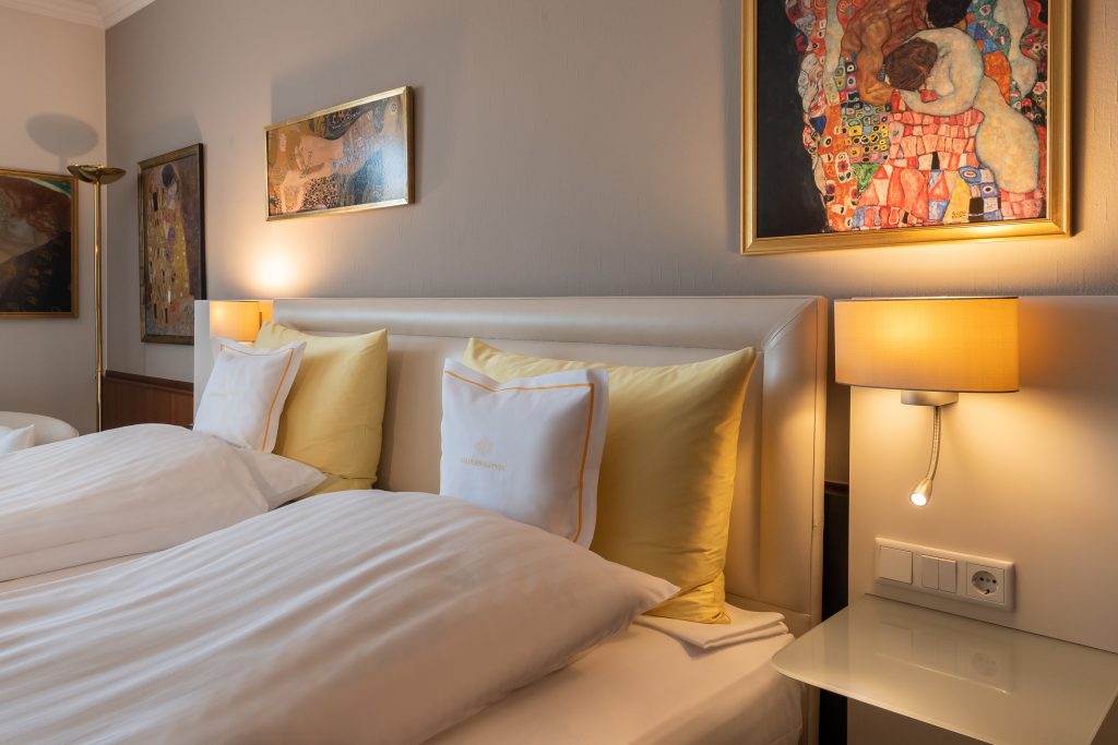Ein ordentlich gemachtes Hotelbett mit gelben Kissen, Wandkunst und warmen Wandlampen auf beiden Seiten.