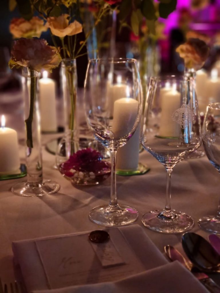 Elegant gedeckter Restauranttisch mit Weingläsern, Kerzen, Blumen und einer Menükarte für ein formelles Abendessen.