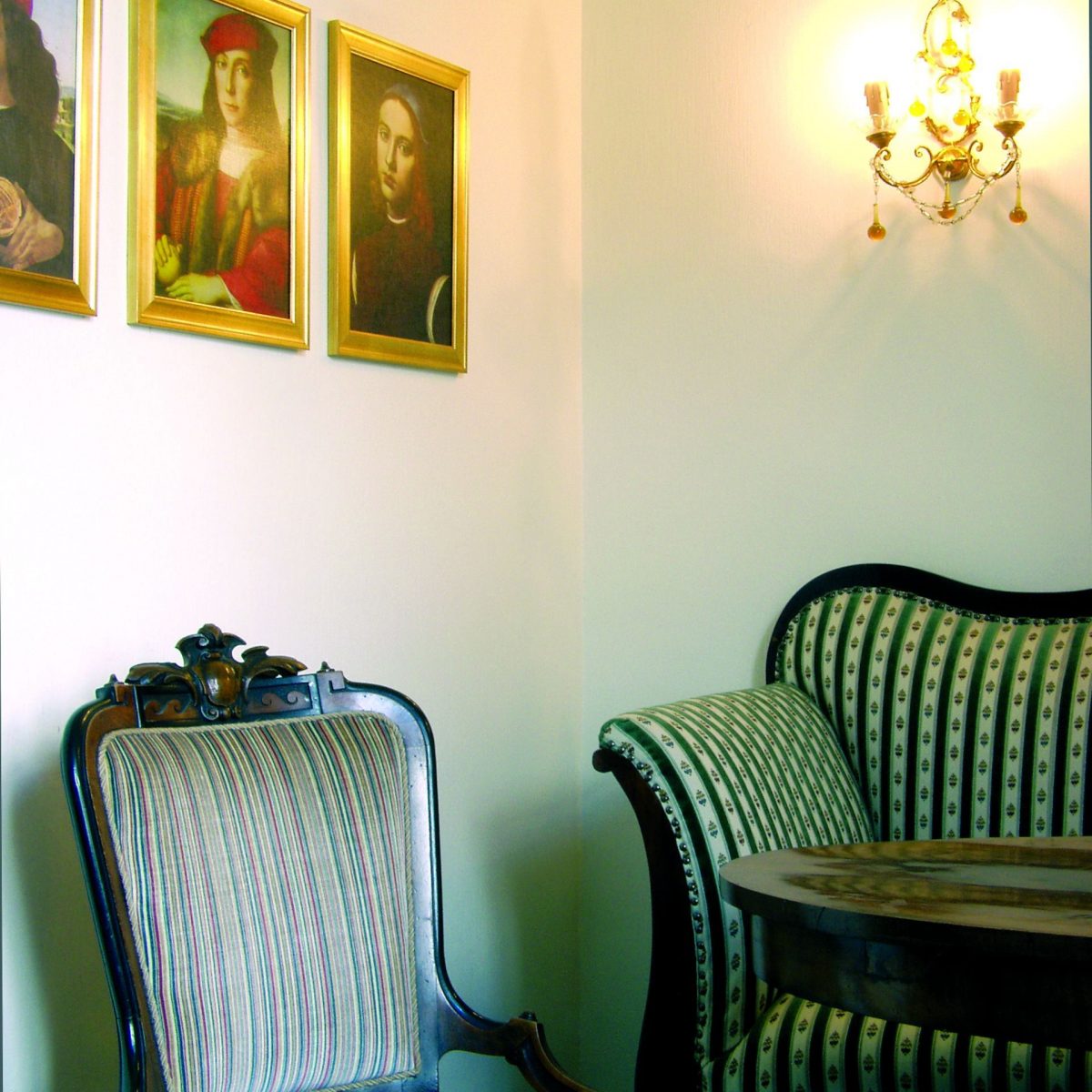 Vintage-Sitzecke mit gestreiften Stühlen, rundem Tisch, Wandkunst und einer beleuchteten verschnörkelten Wandleuchte.